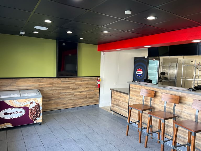 Empty ice cream shop interior with lime green wall, wooden counter, red neon sign, bar seating, and Haagen-Dazs branding visible