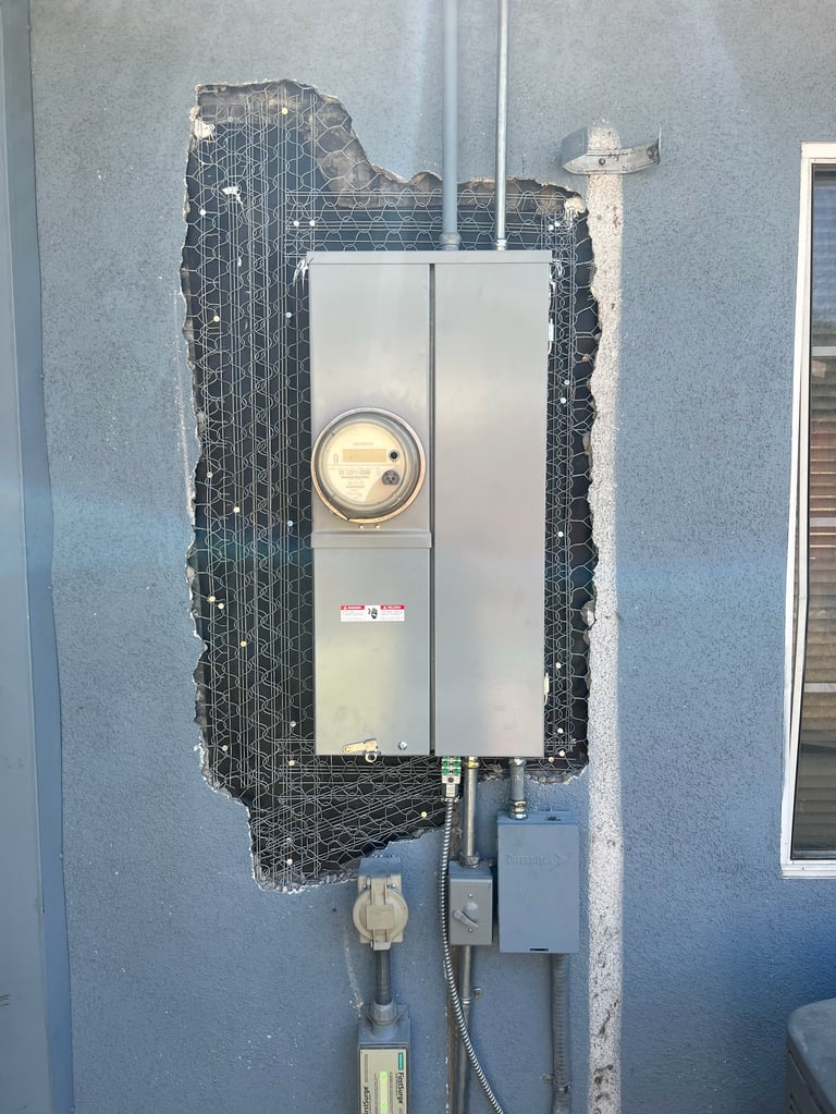 Electrical meter installation on blue wall with protective mesh covering and exposed wiring below