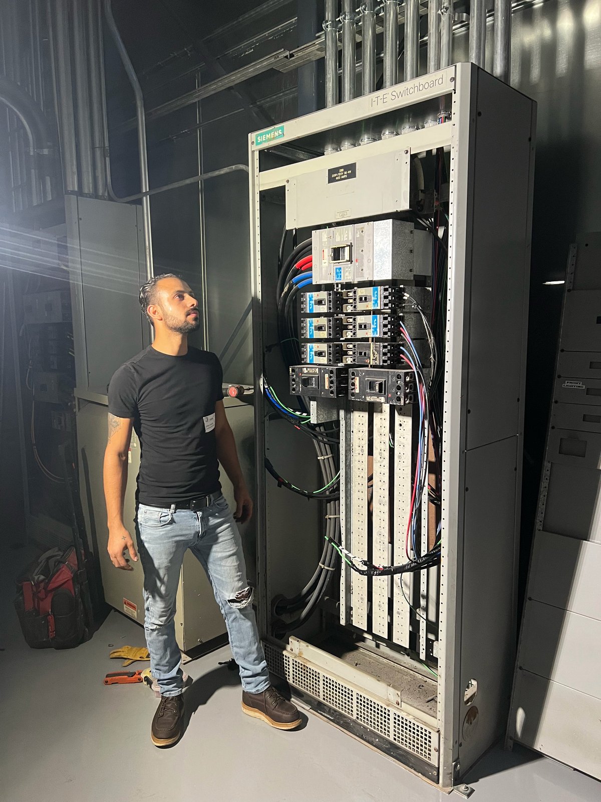 Technician examining electrical panel with circuit breakers and wiring in server room
