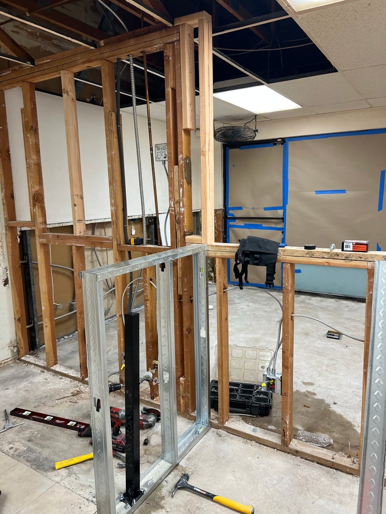 Wooden and metal framed structure under construction in an industrial space with blue tape markings on walls
