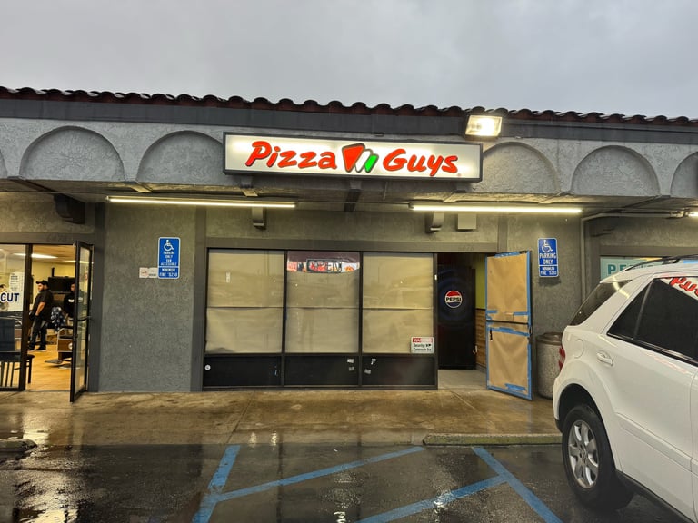 Pizza Guys storefront with illuminated sign, beige facade, and handicap parking spaces in wet conditions