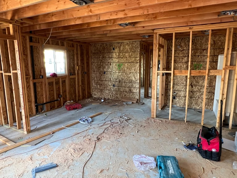 Interior of a home under construction showing exposed wooden framing, insulation, concrete floor, and construction tools