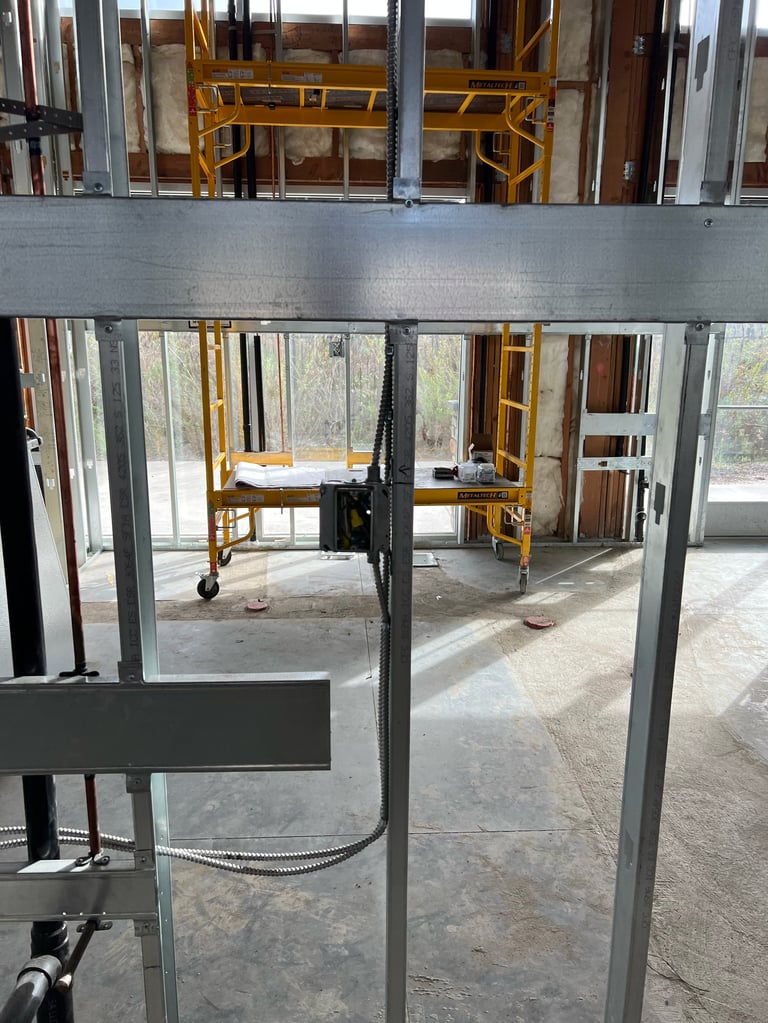 Construction site interior with steel framing, yellow work platforms, and large windows with glass panels