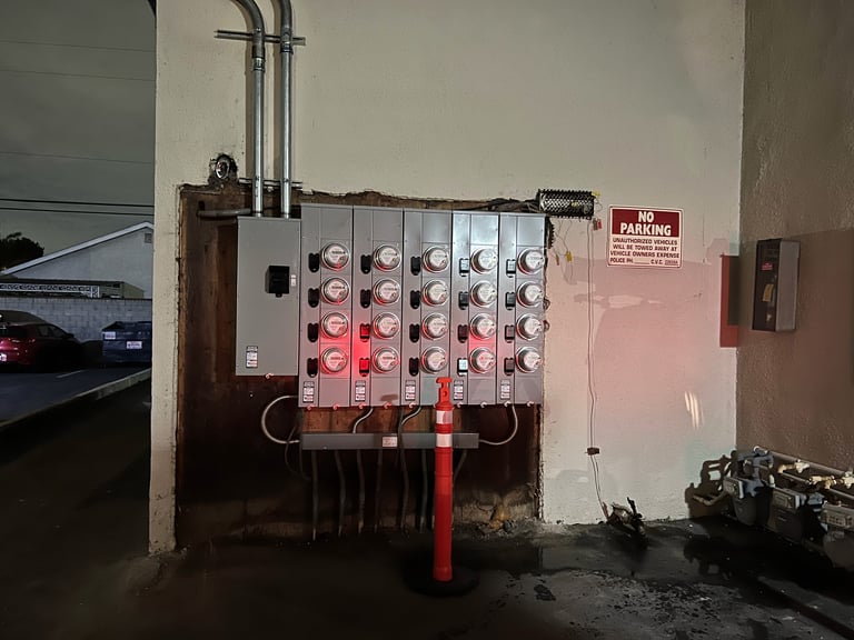 Industrial electrical panel with multiple circuit breakers mounted on a garage wall next to red piping
