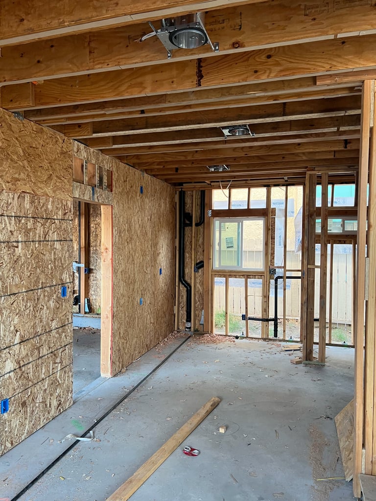 Interior of unfinished residential construction with wooden framing, OSB walls, and large glass doors leading to exterior