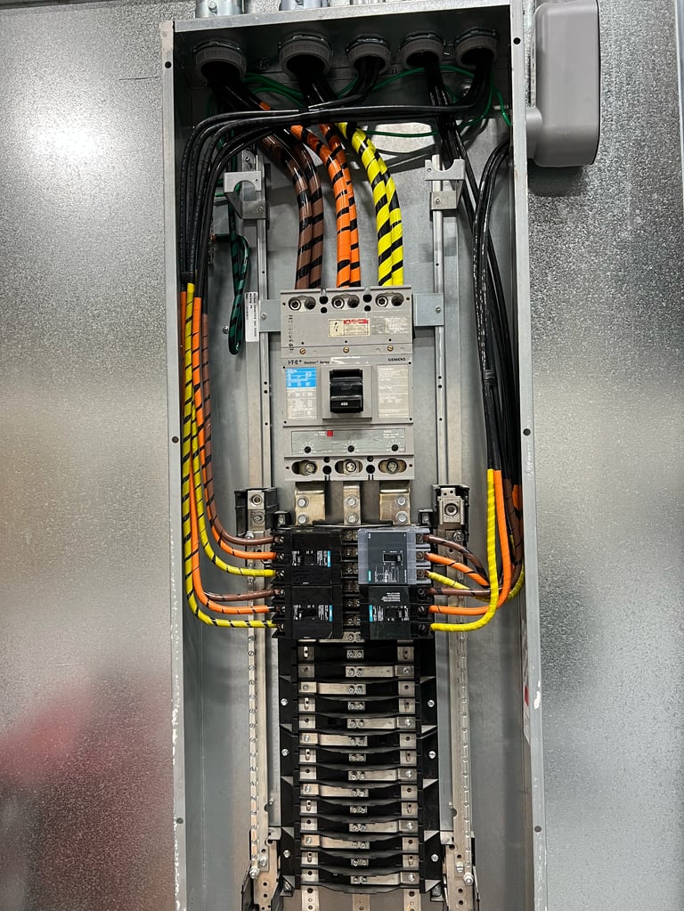 Interior of an electrical panel showing circuit breakers, black and yellow cables, and safety equipment mounted in a metal enclosure