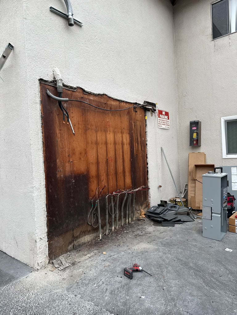 Weathered brown metal door with hanging chains on white wall next to electrical equipment and storage boxes