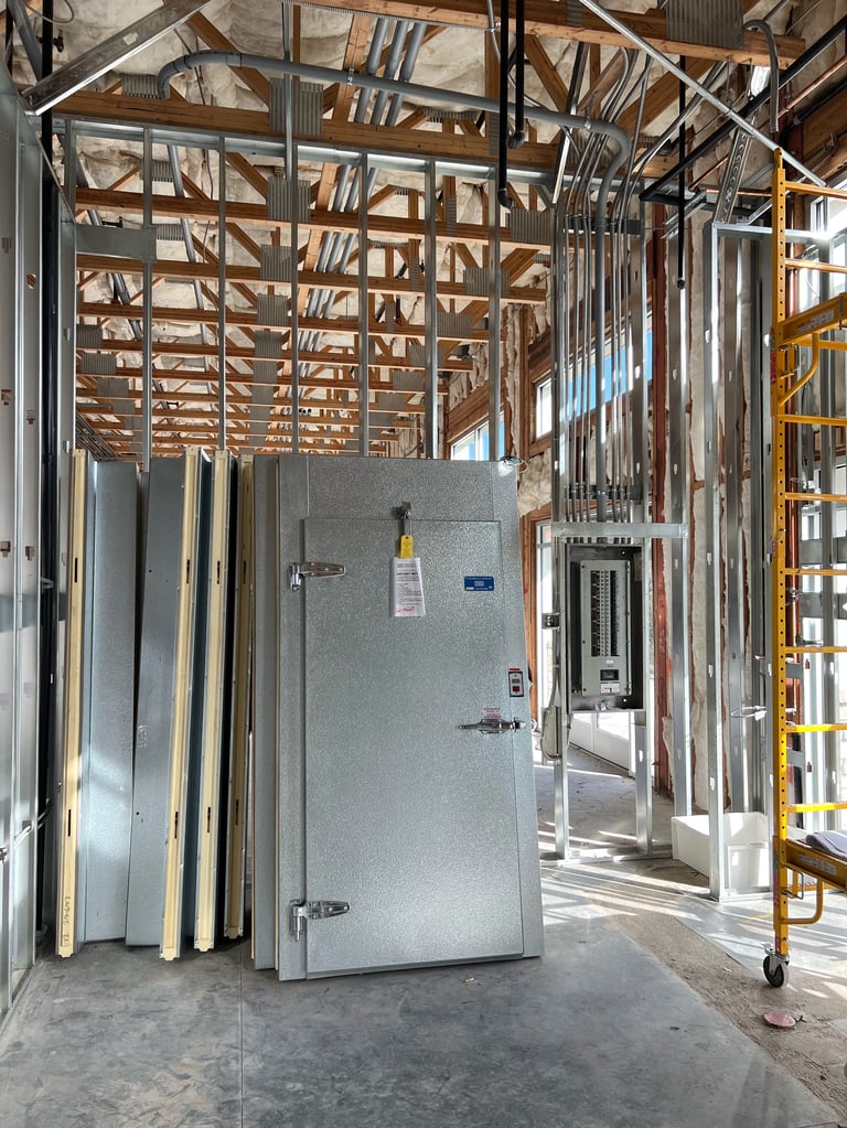 Industrial construction site showing metal stud framing, drywall panels, and a large HVAC unit under wooden roof structure