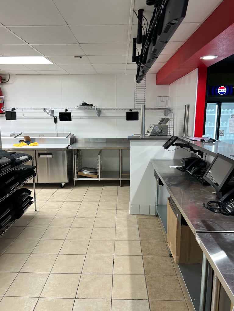 Empty commercial kitchen with stainless steel equipment, prep tables, drop ceiling with mounted TV, and red accent wall
