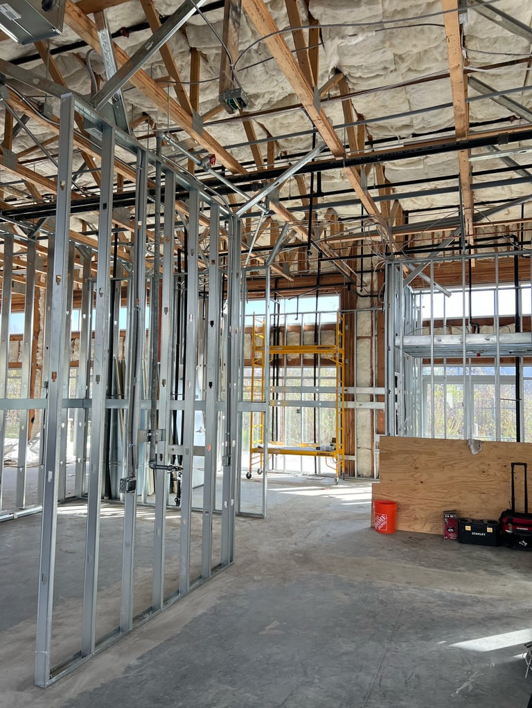 Interior of building under construction with metal framing, wooden beams, drywall, and windows during renovation