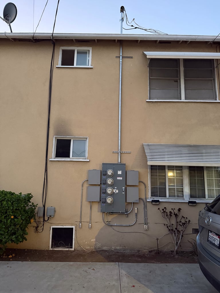 Tan-colored residential building with electrical meters and fuse boxes mounted on exterior wall