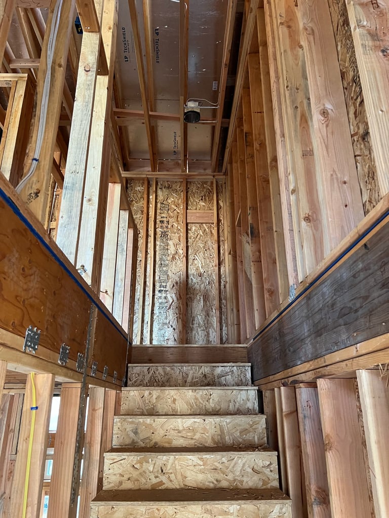 Interior view of wooden staircase under construction surrounded by various wooden door frames and materials