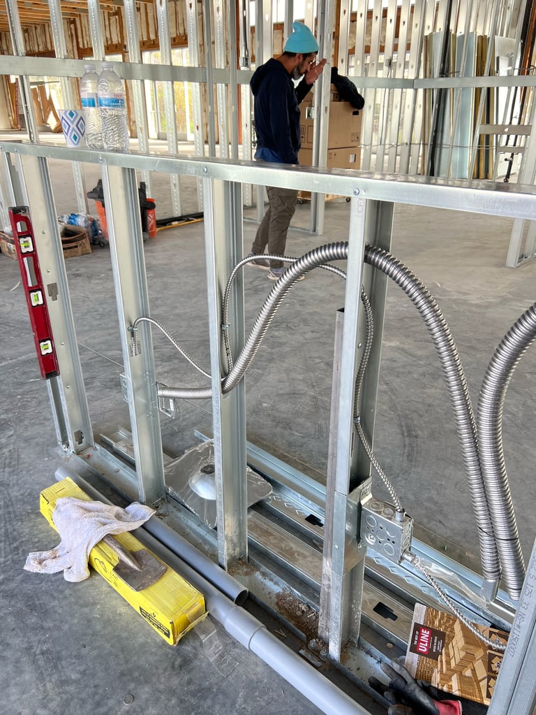 Construction worker in blue hard hat installing framed drywall interior walls with metal studs and flexible ductwork visible