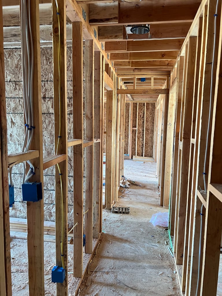 Interior of building under construction showing wooden framing, studs, and insulation along a long hallway perspective